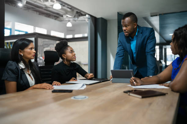 Young African businessman talking with a diverse group of female colleagues during a meeting around a table in an office boardroom